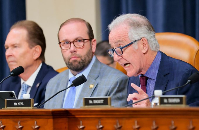 Three men in suits are seated at a congressional hearing table with nameplates reading 'Mr. NEAL' and 'Mr. DOGGETT' visible, with an older man speaking into a microphone.