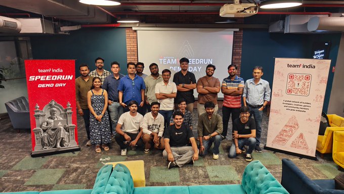 Group photo of the Team India Speedrun Demo Day participants standing and sitting in an office space, flanked by 'team india SPEEDRUN DEMO DAY' banners and a small statue.