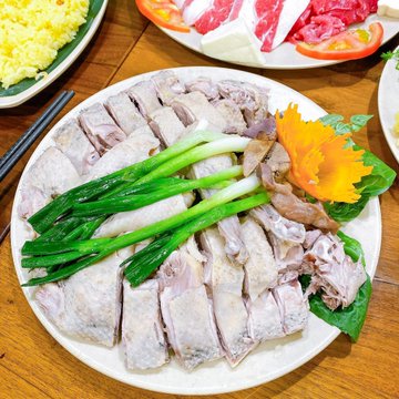A plate of sliced boiled meat garnished with green onions and an orange flower, with other dishes partially visible in the background.
