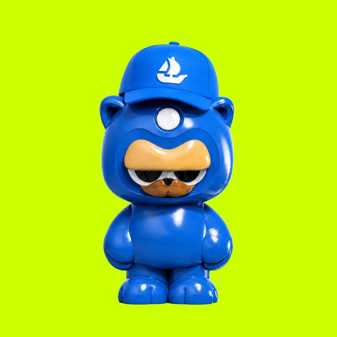 A blue designer toy figure of a bear-like character wearing a cap with a sailboat logo against a lime green background.