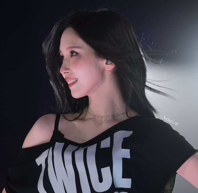 A close-up photo of a smiling young woman with long black hair wearing a black off-shoulder top that reads 'NICE,' with a small heart drawn near her cheek labeled 'wei♡'.