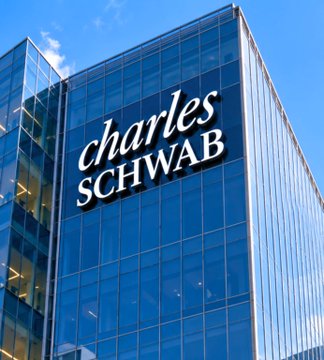 A modern glass office tower displays the "Charles Schwab" logo prominently in white lettering against the blue-tinted windows, matching the financial firm's branding referenced in the article about the company's optimistic stance on a U.S. Strategic Bitcoin Reserve bill.