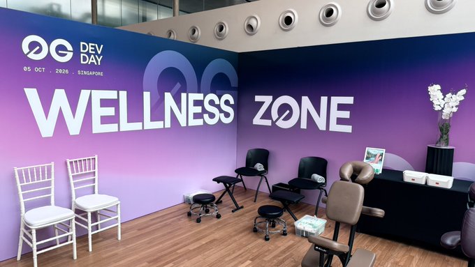 A 'Wellness Zone' event booth with a purple and blue gradient wall, the 'OG Dev Day 05 Oct 2020 Singapore' logo, and several massage chairs and white chairs displayed.