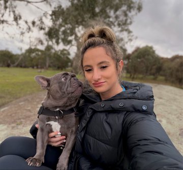 A young woman with her hair in a bun takes a selfie while holding a gray French Bulldog puppy outdoors, with the dog looking away from the camera. The image appears to be a personal moment that contrasts with the post's promotional message about a casino/sportsbook revenue-sharing program called "BC," suggesting the author is balancing everyday life with business activities.