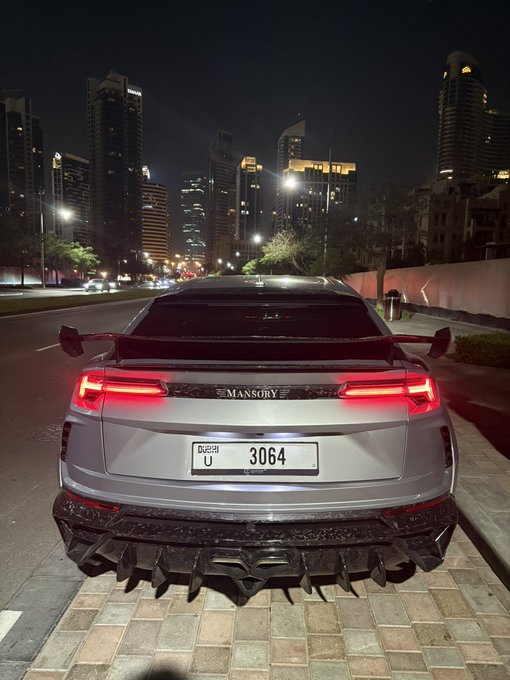 A customized Lamborghini Urus by Mansory with Dubai license plate "U 3064" is parked at night against a city skyline backdrop, likely shared as part of an automotive luxury ("GN") lifestyle post.