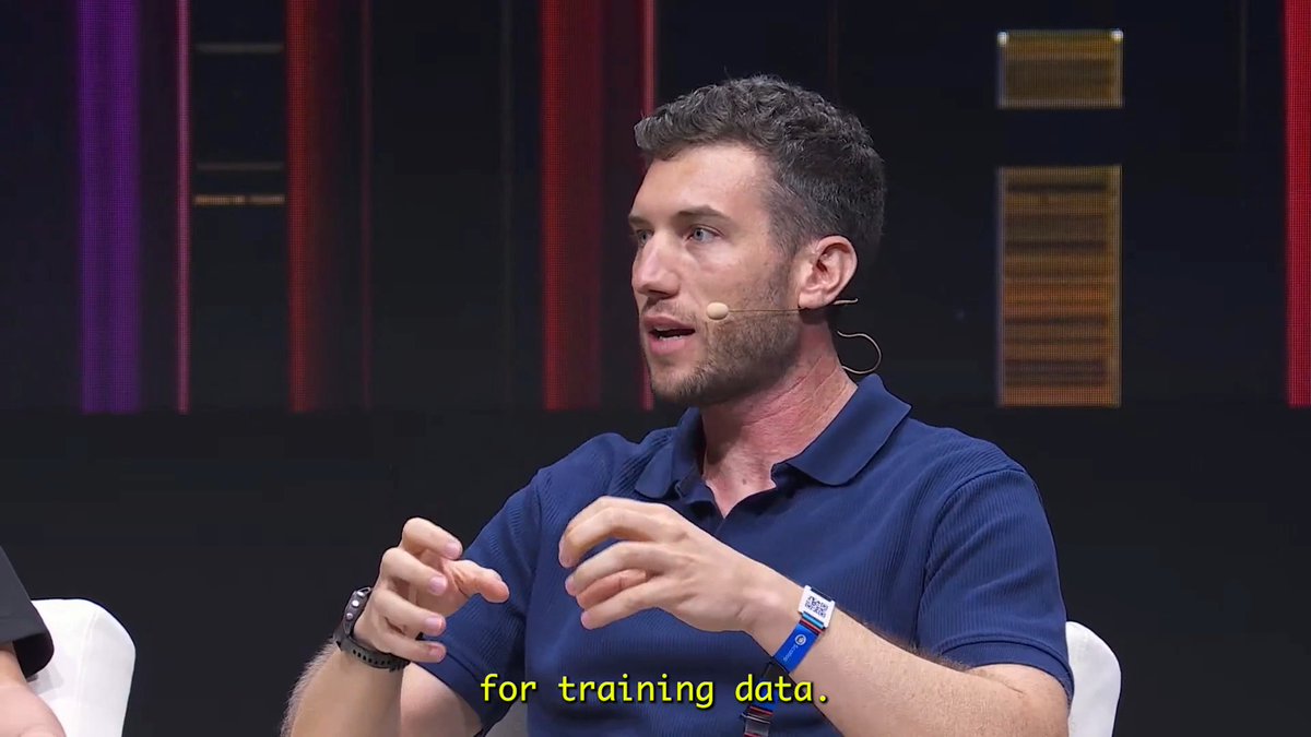 A man in a blue polo shirt speaks on a stage, with the subtitle 'for training data.' visible at the bottom of the frame.