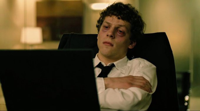 The image shows a man sitting in an office chair with his arms crossed while looking at a laptop computer. The man appears to be tired or bored, possibly taking a break from work or just relaxing during his downtime.