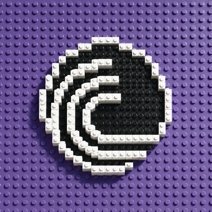 A close-up of a purple Lego baseplate with a stylized 'e' logo built in black and white Lego bricks in the center.