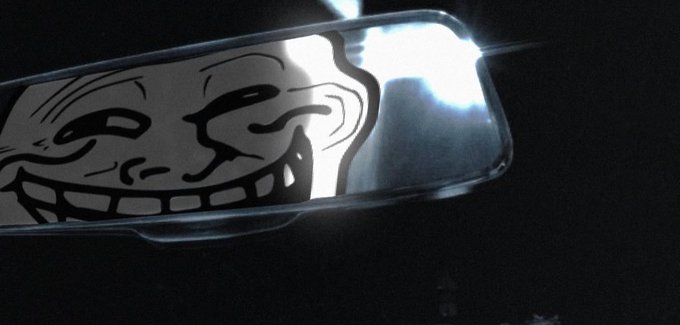 A close-up shot of a silver smartphone case featuring a black and white troll face meme graphic, illuminated by a bright light source against a dark background.