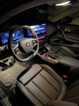 Interior view of a BMW vehicle showing the steering wheel with the BMW logo, digital dashboard displays, and black leather interior at night.