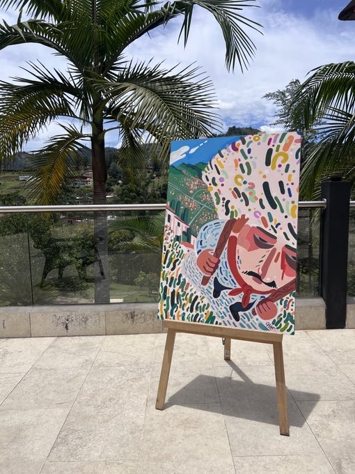 A colorful abstract painting on an easel stands on an outdoor terrace, depicting a figure amid confetti-like shapes with palm trees in the background.