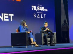 Two people sit in armchairs on a stage during a presentation, with a large screen behind them displaying '78,848 USD' and the word 'SALT' in capital letters.