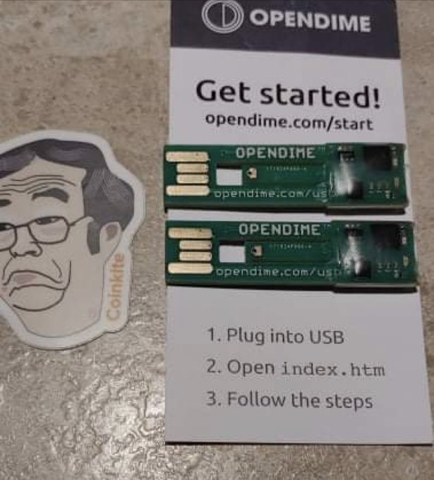 Two OPENDIME USB Bitcoin hardware sticks displayed on a 'Get started!' instruction card, accompanied by a Coinkite sticker featuring a cartoon portrait.