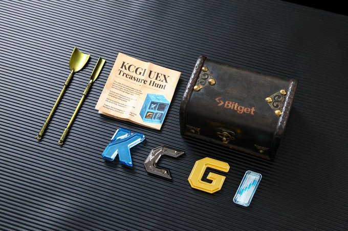 A flat-lay of KCGUEX and Bitget branded merchandise on a black ribbed surface, including golden cutlery, a Treasure Hunt card, a vintage-style treasure chest, and colorful KCGU letter pins.
