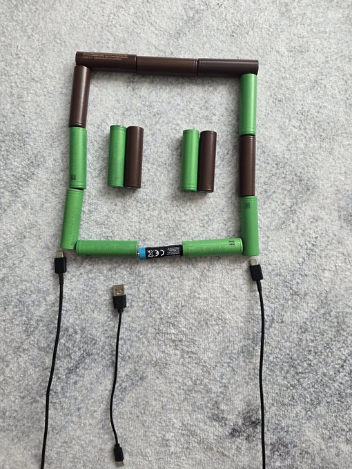 A creative arrangement of green and brown AA batteries with USB cables connected, configured to form a shape resembling a smiling face on a gray surface.
