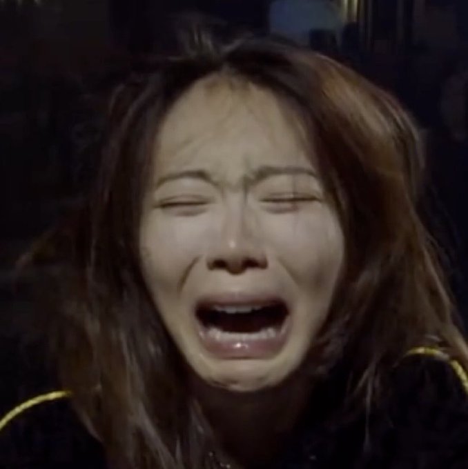A close-up of a woman crying with her eyes closed and mouth open in an expression of distress, with long brown hair framing her face.