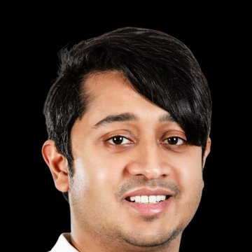 The image features a man with black hair wearing a white shirt who has a big smile on his face. The background of the image is black, which makes him stand out more against this backdrop. There are no other objects or texts present in the image.