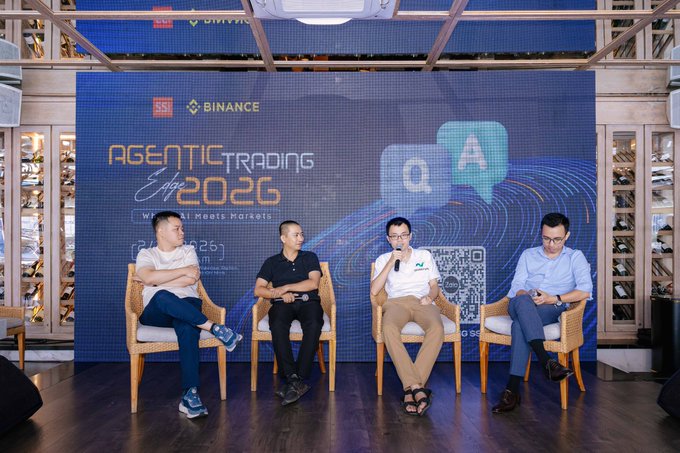 Four men sit on chairs on a stage at a Binance 'AGENTIC TRADING 2026: When AI Meets Markets' event, with one man speaking into a microphone.