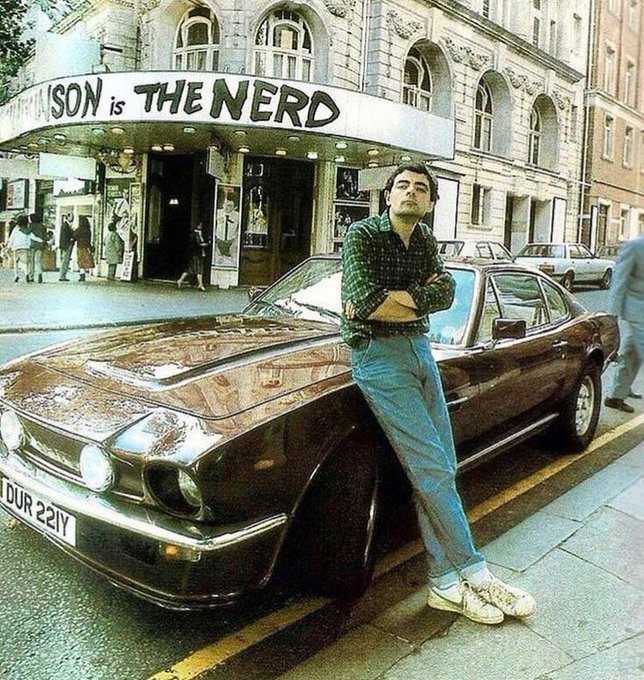 A man leans against a vintage car in front of a theater marquee that reads 'SON is THE NERD,' styled as an edit of the classic 'John is the Nerd' meme.