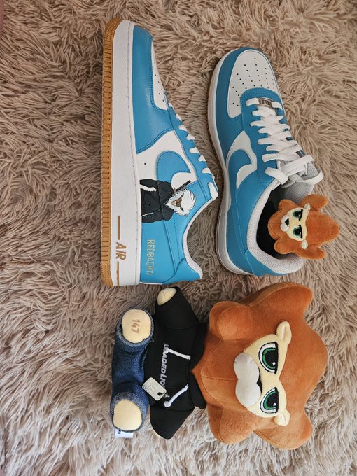 A pair of blue and white Nike Air Force 1 Low sneakers are displayed on a fluffy beige rug alongside black MZEC socks and an orange Loaded Lions plush head accessory, showcasing a creative "Loaded Lions" themed outfit. The "AIR" and "RIDEAOMES" text visible on the shoes complements the post's celebration of community members styling the NFT collection.