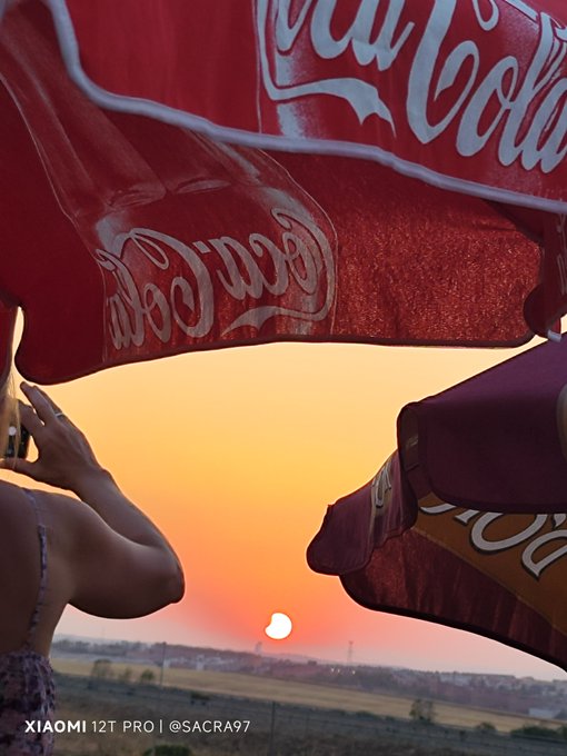 Two Coca-Cola hats with people wearing them in front of a sunset, with watermark 'XIAOMI 12T PRO | @SACRA97'.