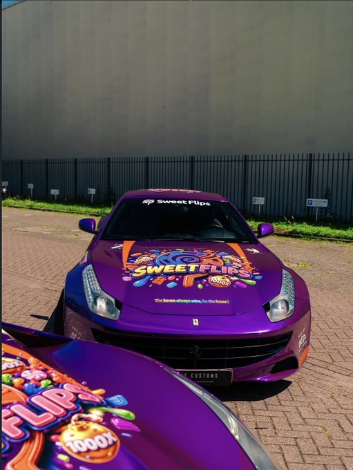 A vibrant purple Ferrari sports car branded with colorful "SweetFlip" candy-themed graphics and the tagline "The house always wins, by the house!" sits parked on a brick driveway, with a second matching vehicle visible in the foreground. The branded wrap design aligns with the SweetFlips promotional post, showcasing the casino/candy brand's flashy aesthetic as the team greets followers and offers USDT/ETH crypto tips for Sunday.