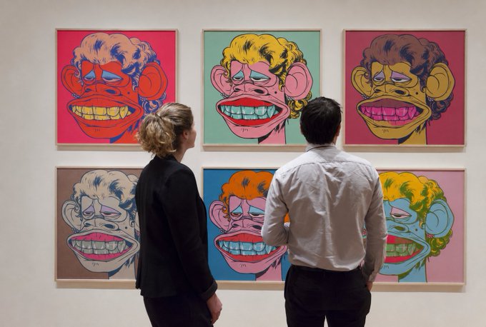 Two people viewing an art installation featuring six colorful pop-art portraits of monkeys with prominent teeth, reminiscent of KAWS style.