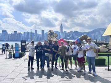 The image shows a group of people posing for a photo, with some holding up their cell phones or cameras. The backdrop features a city skyline, indicating that they are at an urban location. The caption reads "I am a Bored Ape I am part of the best Club on the internet. I celebrate the community we've built." This message seems to be related to the group's gathering and the context of their photo session in front of the cityscape.