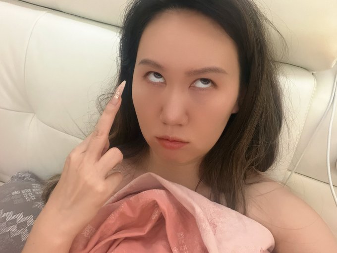 A young woman lies on a white leather couch, rolling her eyes upward and pointing at her temple with a decorated fingernail, her expression conveying exasperation or disbelief that mirrors the post's commentary on the chaotic MEME stock situation involving Four_FORM's resistance to Robinhood.
