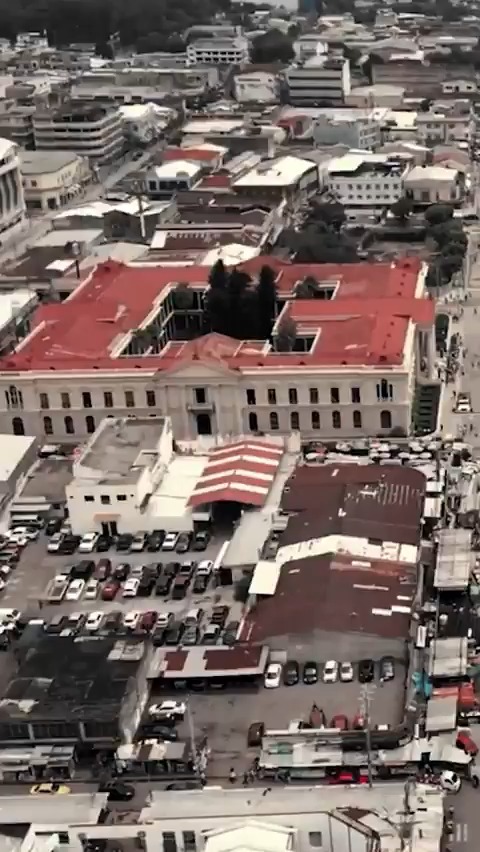 An aerial view of a government building complex with a distinctive red roof in an urban setting, surrounded by busy streets and parking areas. The image likely represents El Salvador's civic infrastructure, visually reinforcing the post's bullish sentiment about the country's development and progress.