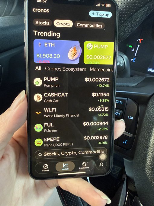 A hand holds a smartphone in a car displaying the Cronos crypto app with trending tokens including ETH at $1,908.30 and PUMP at $0.002672, along with PUMP, CASHCAT, WLFI, FUL, and kPEPE listed below.