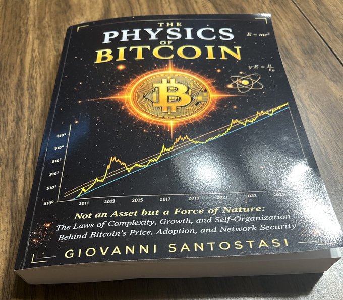 A book titled "The Physics of Bitcoin" by Giovanni Santostasi, with the subtitle "Not an Asset but a Force of Nature," resting on a wooden table.