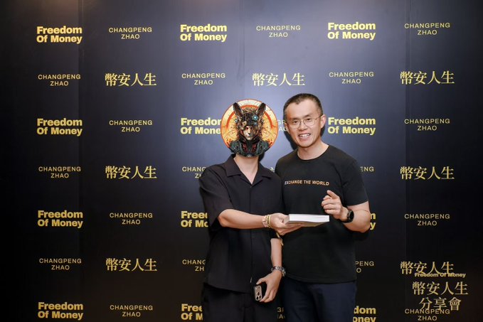 Two men pose together at a "Freedom Of Money" book-sharing event in Hong Kong, with one wearing a black button-up shirt and the other in a "Change The World" t-shirt, standing before a backdrop covered in "Freedom Of Money" and "CHANGPENG ZHAO" branding alongside a wolf graphic. The post reflects on the author's first photo with CZ (Changpeng Zhao), highlighting his late-career success with Binance at age 39-40 and his philosophy of calculating whether he can afford to lose before placing big bets.