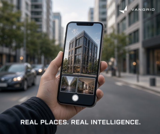 A hand holding a smartphone displaying an AR view of a building on a city street, branded with the VANGRID logo and the tagline 'REAL PLACES. REAL INTELLIGENCE.'