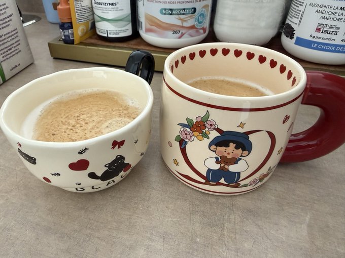A charming pair of coffee mugs—one decorated with a black cat design and the other featuring a sailor figure inside a floral heart—sit on a counter filled with coffee creamer bottles. The mugs, containing frothy coffee, tie into the $XRP Army post by inviting viewers to "rate" the morning cups as a fun, community engagement prompt.