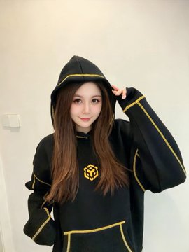 A young woman wearing a black hooded sweatshirt featuring the Binance logo poses indoors, showing off the freshly unboxed merchandise she received from the crypto exchange. The post thanks Binance's Chinese accounts (@binancezh, @heyibinance) and CZ (@cz_binance) for the gift.