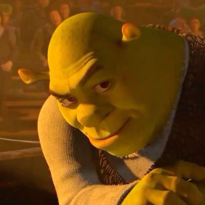 A 3D-rendered image of Shrek looking sideways with a skeptical or sly expression, wearing his signature tunic, with a crowd visible in the background.