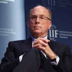 A man in a suit with glasses sits with clasped hands at what appears to be the Institute of International Finance (IIF), listening attentively.