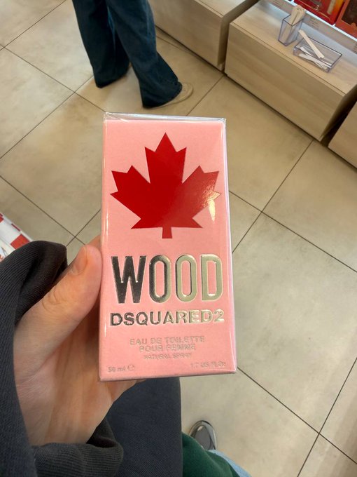 A hand holds a pink box of Dsquared2 "WOOD" Eau de Toilette Natural Spray (30 ml), likely the favorite perfume purchased with a crypto WEB3 card during a recent international trip.