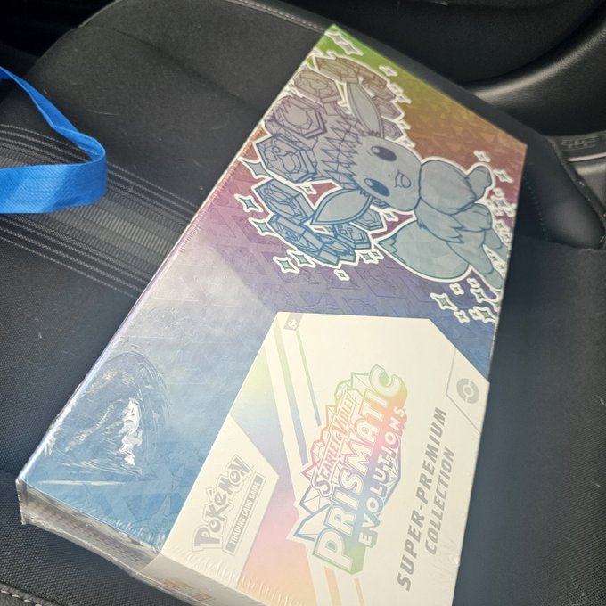A sealed Pokémon TCG **“Prismatic Evolutions Super-Premium Collection”** box featuring a Shiny Ditto illustration is shown on a car seat. The accompanying post claims this product could be worth over **$2,000 by 2027**.