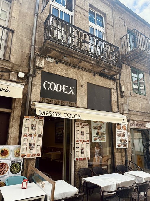 Exterior of 'CODEX Restaurante / Mesón Codex' restaurant with menu displays and outdoor seating tables on a stone street corner.