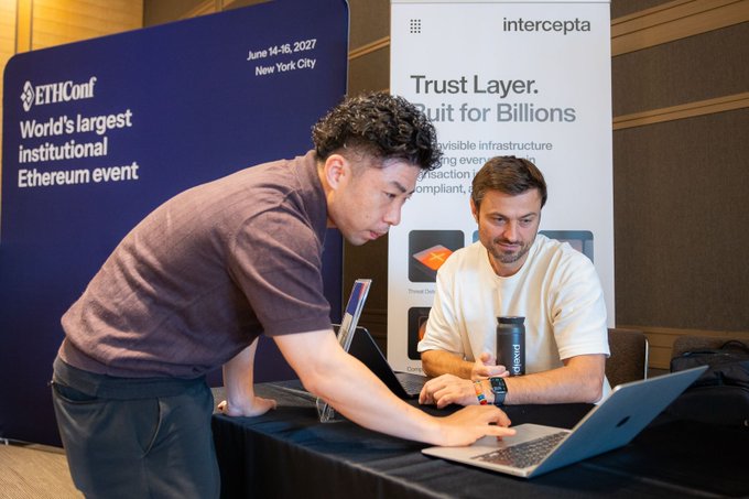 Two men look at a laptop at a booth with banners reading 'ETHConf' ('June 14-16, 2027, New York City, World's largest institutional Ethereum event') and 'Intercepta' ('Trust Layer. Built for Billions').