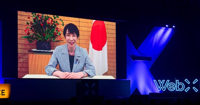 Japanese Prime Minister Sanae Takaichi speaks at WebX 2026, reaffirming support for startups and Web3. The image shows Takaichi on a screen behind the "WebX" logo.