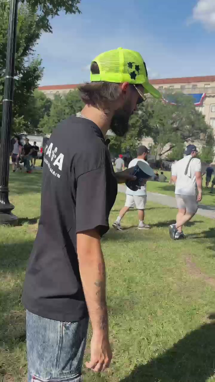 The image shows a man wearing a black t-shirt, blue jeans, and a neon green hat standing in a park with other people around him. The photo also contains text that reads "The Aliens Have Invaded DC. Live From UFC FREEDOM 250! @SolJakey & @TheArtOfWarren". This post seems to be promoting an event or gathering related to the recent protests against police brutality and racism, as indicated by the reference to the "Aliens Have Invaded DC." The man in the image appears to be a part of this event or gathering.