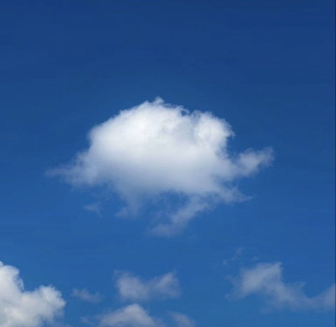 A photograph of a single fluffy white cloud against a clear blue sky, with smaller clouds visible near the bottom edges.