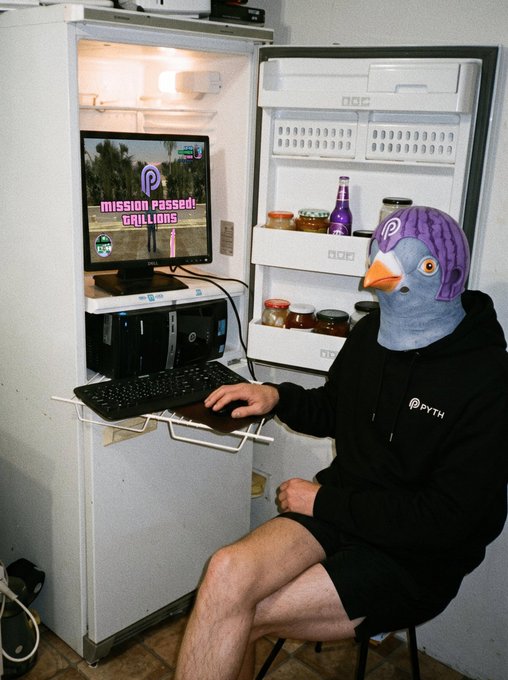 A person wearing a Pyth Network hoodie and a purple pigeon mask sits at a computer in front of an open refrigerator, with the monitor displaying 'MISSION PASSED! GRILLIONS'.