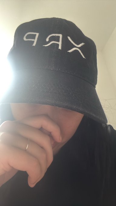 A person wearing a black corduroy cap with 'KARL' embroidered in white letters covers the lower half of their face with their hand, which bears a simple silver ring.
