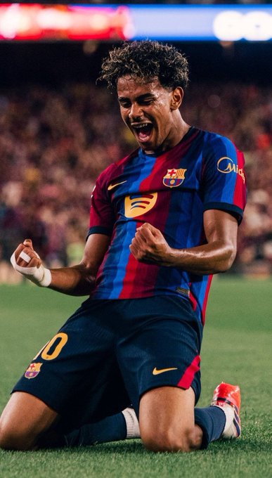 A young FC Barcelona player wearing the iconic blue and red striped jersey with the number "10" on his shorts kneels on the pitch with his fists clenched and mouth open in an exuberant celebration, embodying the Blaugranas' 🔴 passion and hope as they chase La Liga glory with a 60% chance to win the league per Polymarket, ready to capitalize on Real Madrid's dropped points at Real Betis.