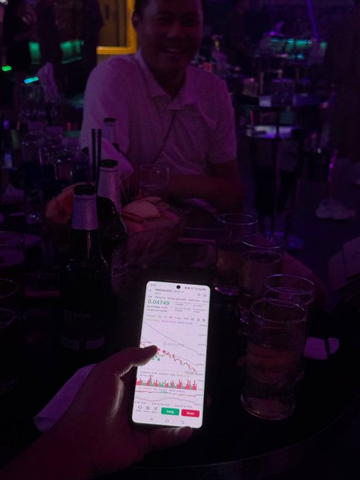 The image features a person holding up their smartphone displaying an economic graph or chart with a downward sloping line, possibly representing a decrease in stock prices. The smartphone is positioned near several glasses of water placed on a dining table.