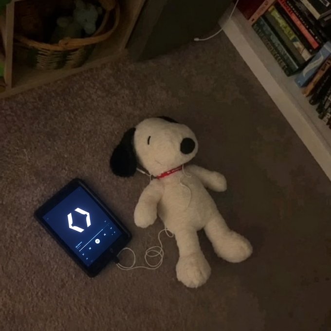 A Snoopy plush toy lies on carpet next to a small screen displaying the number '0' in a digital font, with white earbuds resting on the toy.